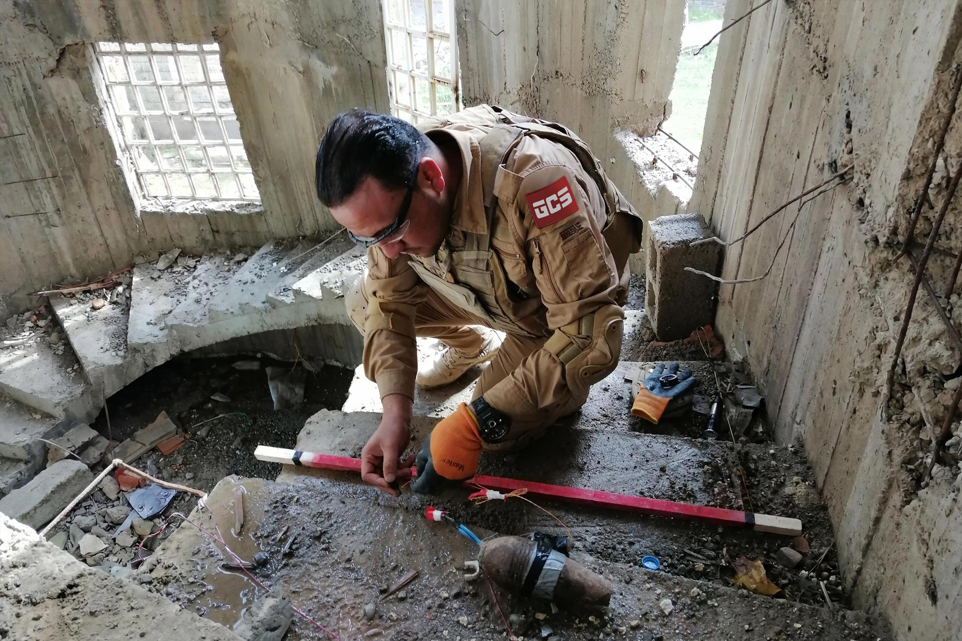 GCS EOD operator handling IED components inside a damaged building during urban clearance training operations in Iraq.