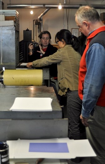 A photo of a person is working at a printing press while other people are watching or filming.