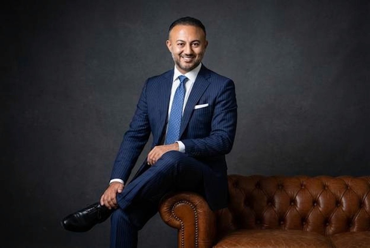Yusuf Yaran in blue suit seated on leather sofa during professional studio portrait session.