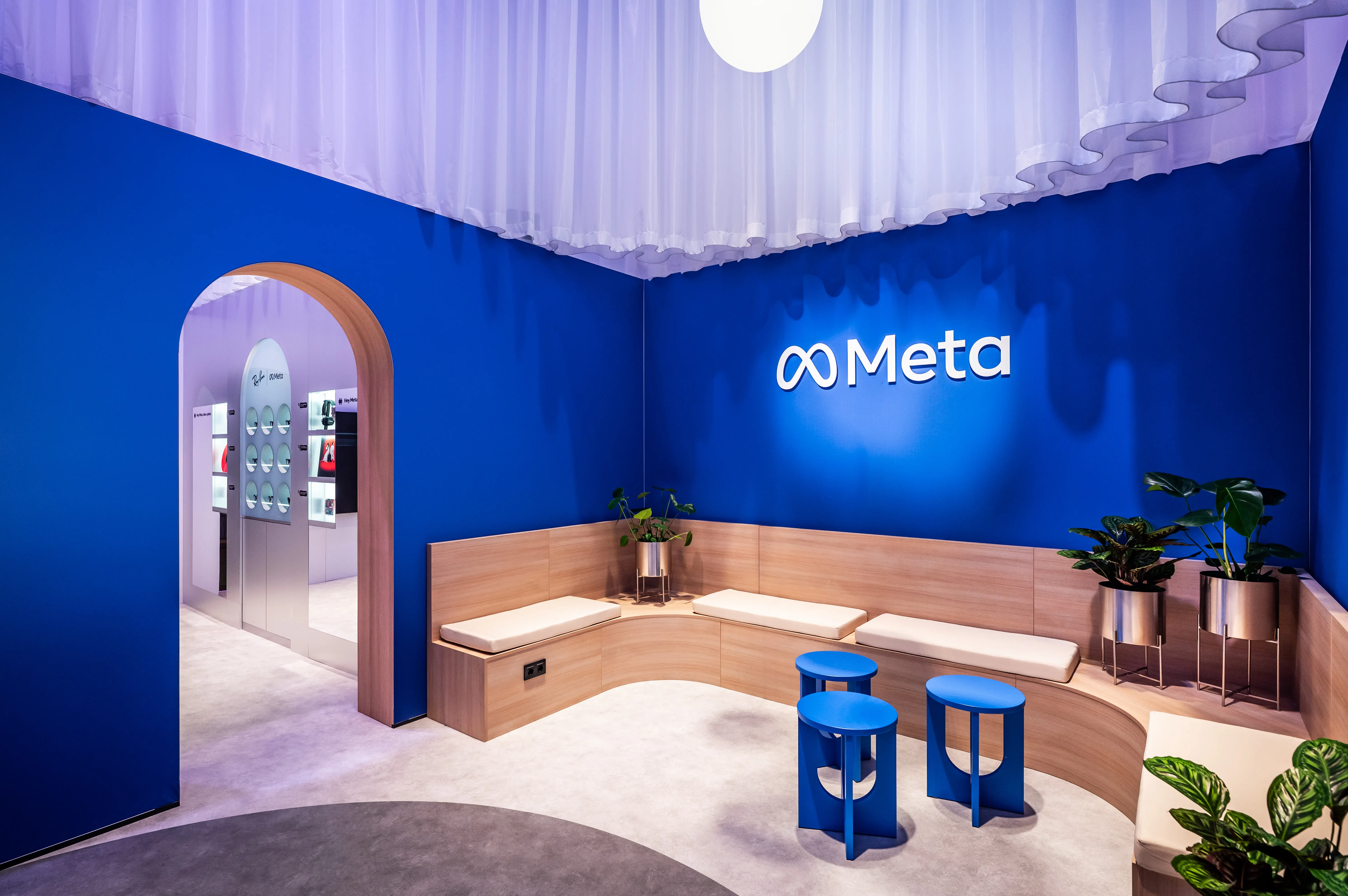 Blue seating area with glowing Meta logo, wooden bench seating, blue stools and ruffled curtain ceiling.