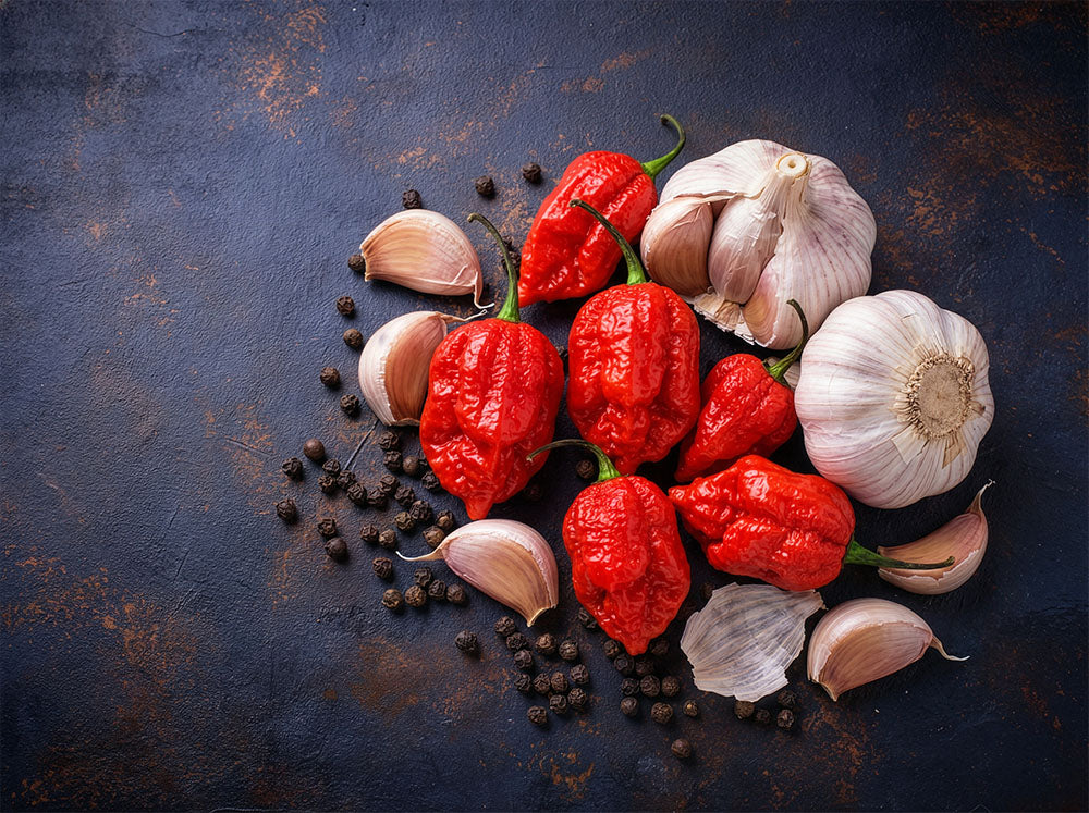 Red ghost peppers and garlic cloves on a dark textured surface.