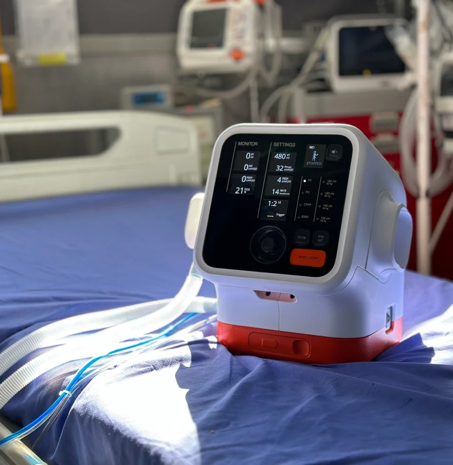 Medical ventilator device with digital display showing vital settings and monitoring data, positioned on hospital bed ready for patient care.