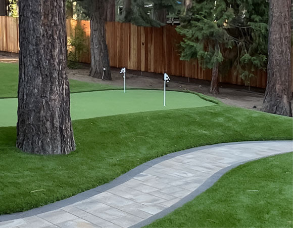 A path cuts between two lush green AGL Grass lawns leading to a Golf Leisure putting green for golfers.
