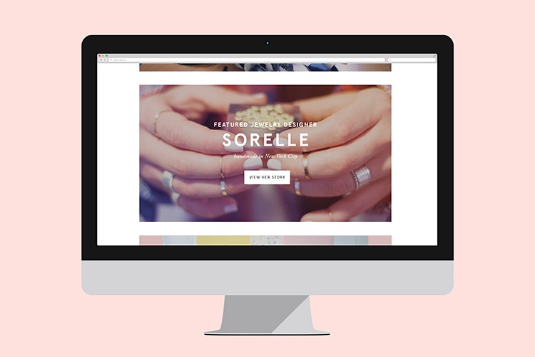 A silver Apple iMac computer displays a webpage titled “FEATURED JEWELRY DESIGNER SORELLE” with the subtitle “handmade in New York City.” The webpage features a background image of hands holding jewelry and a “VIEW HER STORY” button. The computer is positioned against a light pink background.