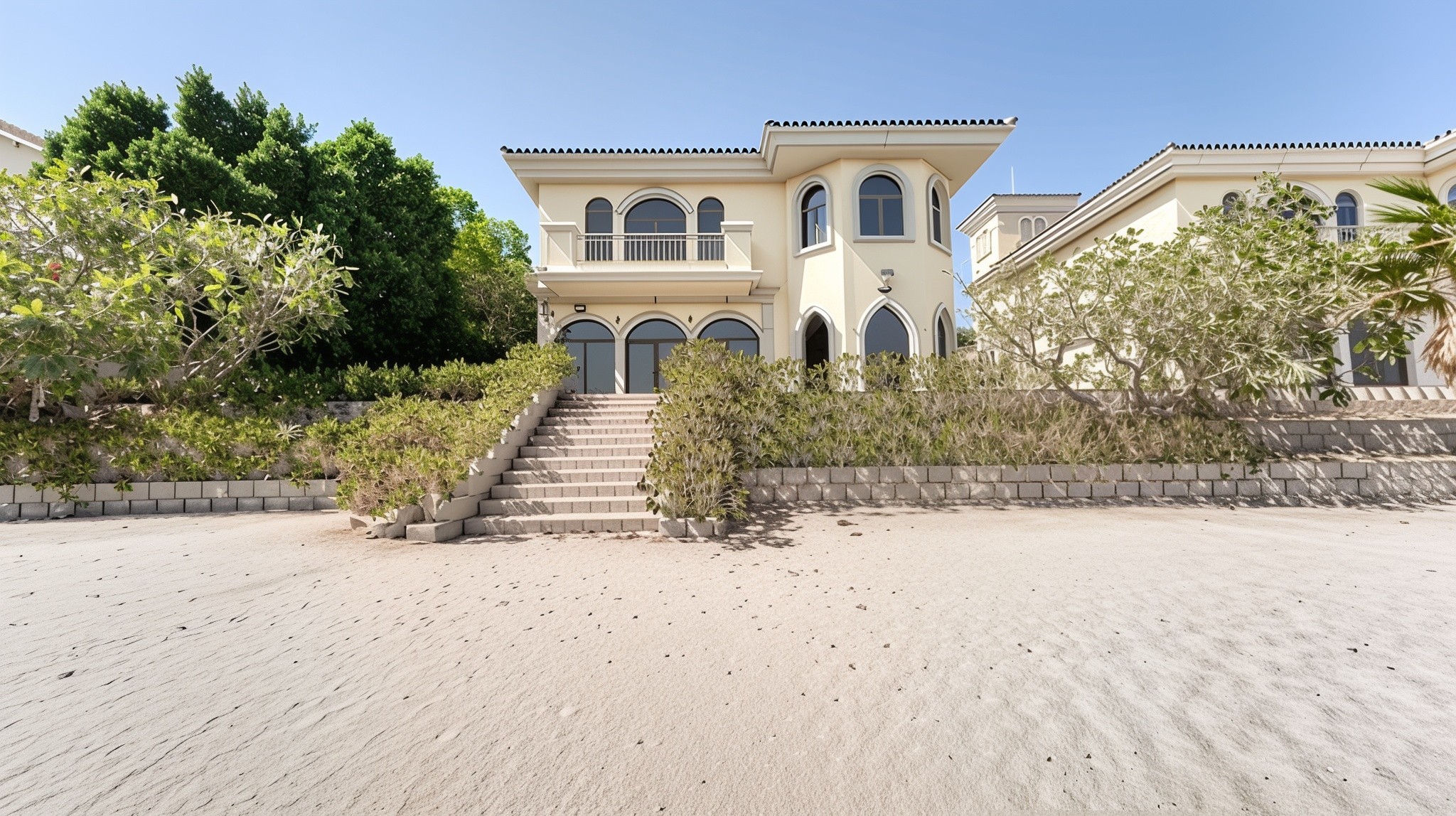 A large beachside house with steps leading to the shore, surrounded by beautiful garden homes.