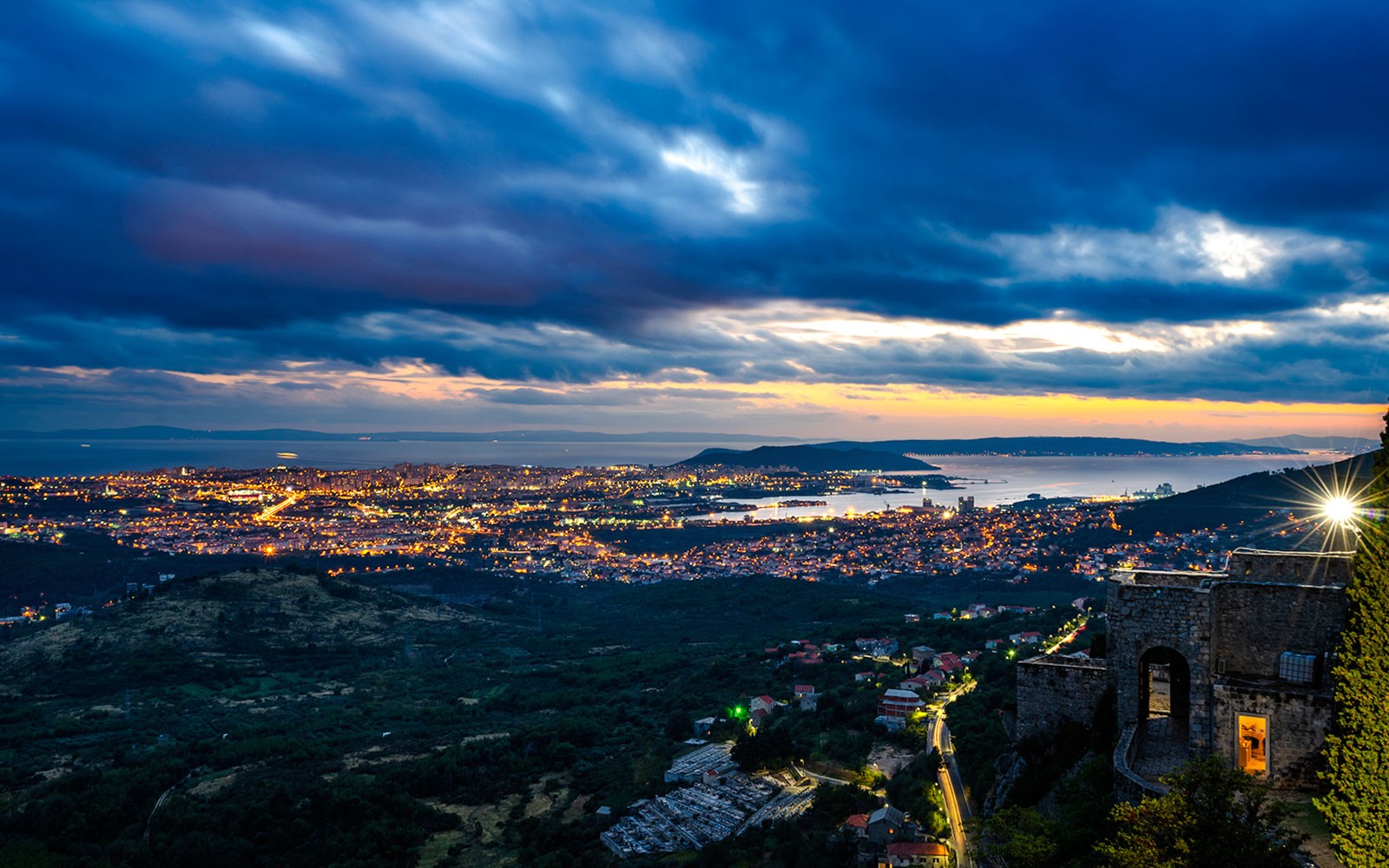 Fortezza di Klis al tramonto con vista su Spalato, Croazia, illuminata dalle luci della città.