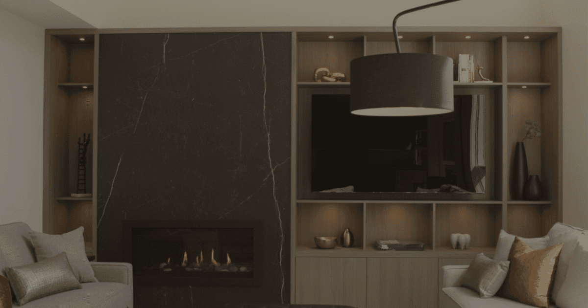 Living room with built in millwork and entertainment area. To the left, a gas fireplace illuminates the room. It is cladded in a single piece of dark marble look engineered stone.
