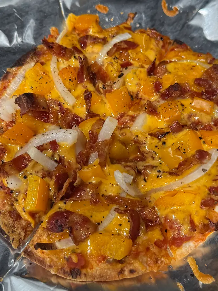 Homemade personal pizza on a toasted wrap with cheese, onions, peppers, and bacon.