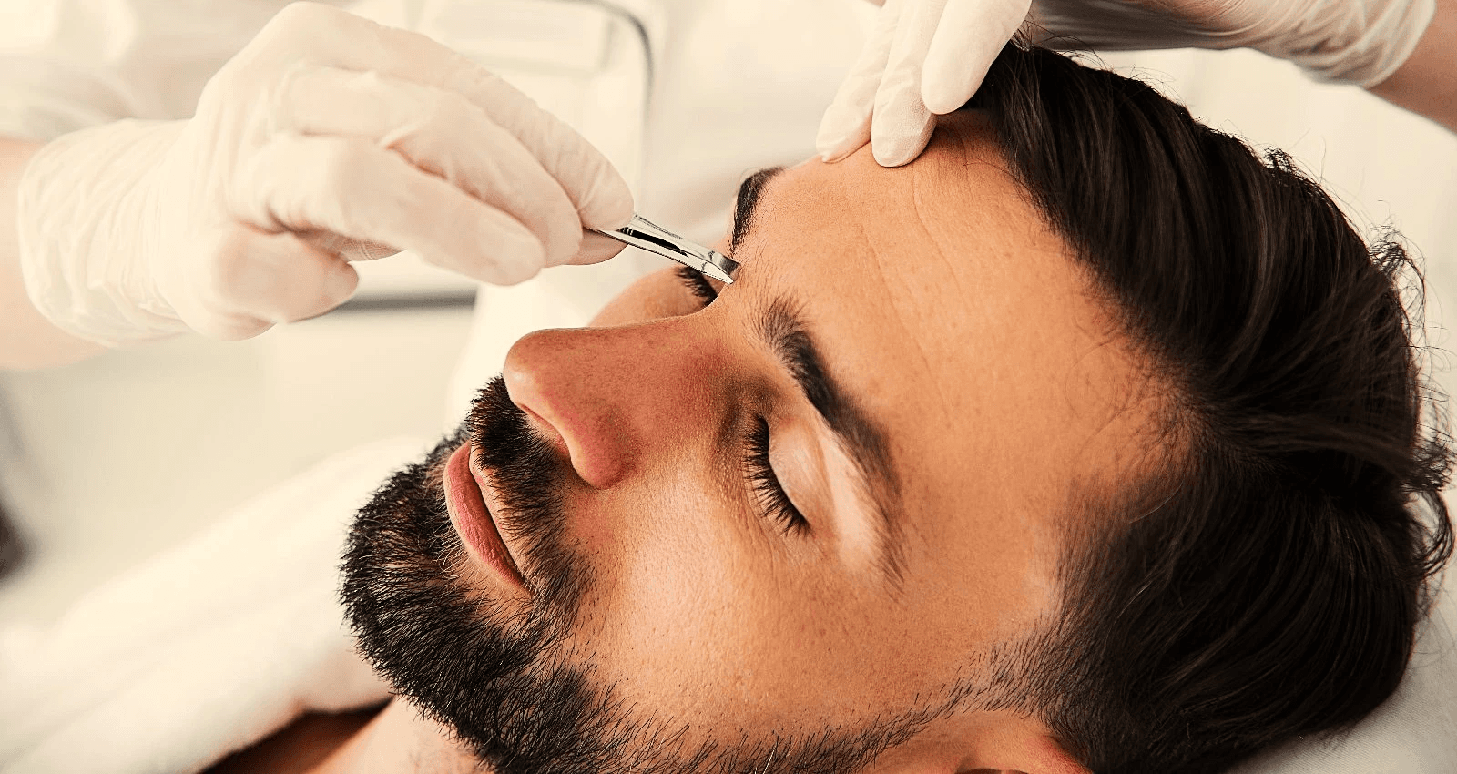 A man relaxes with a facial treatment, wearing a black eye mask, as a gloved hand applies a product.