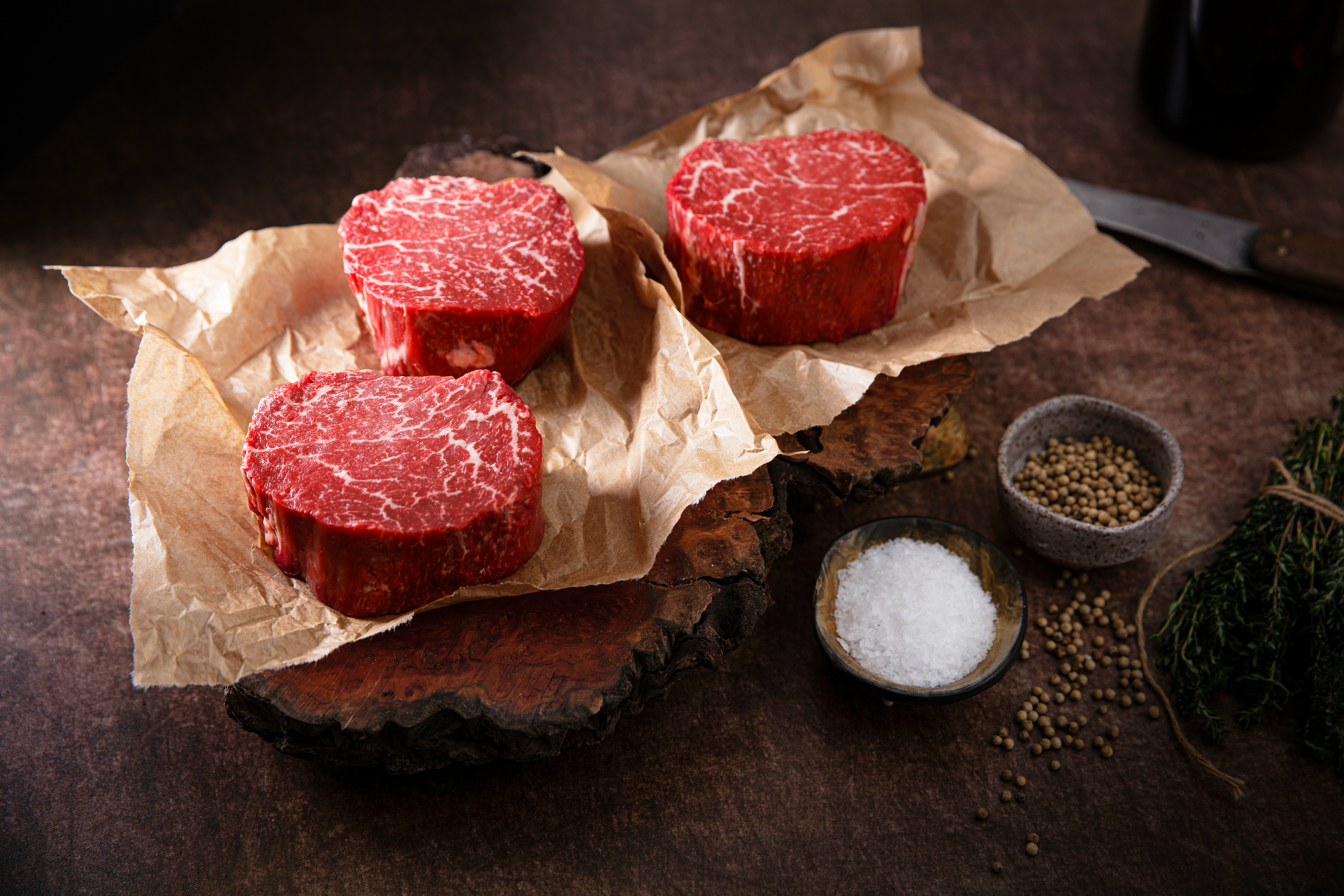 Raw steaks wrapped in brown butcher paper on a dark table