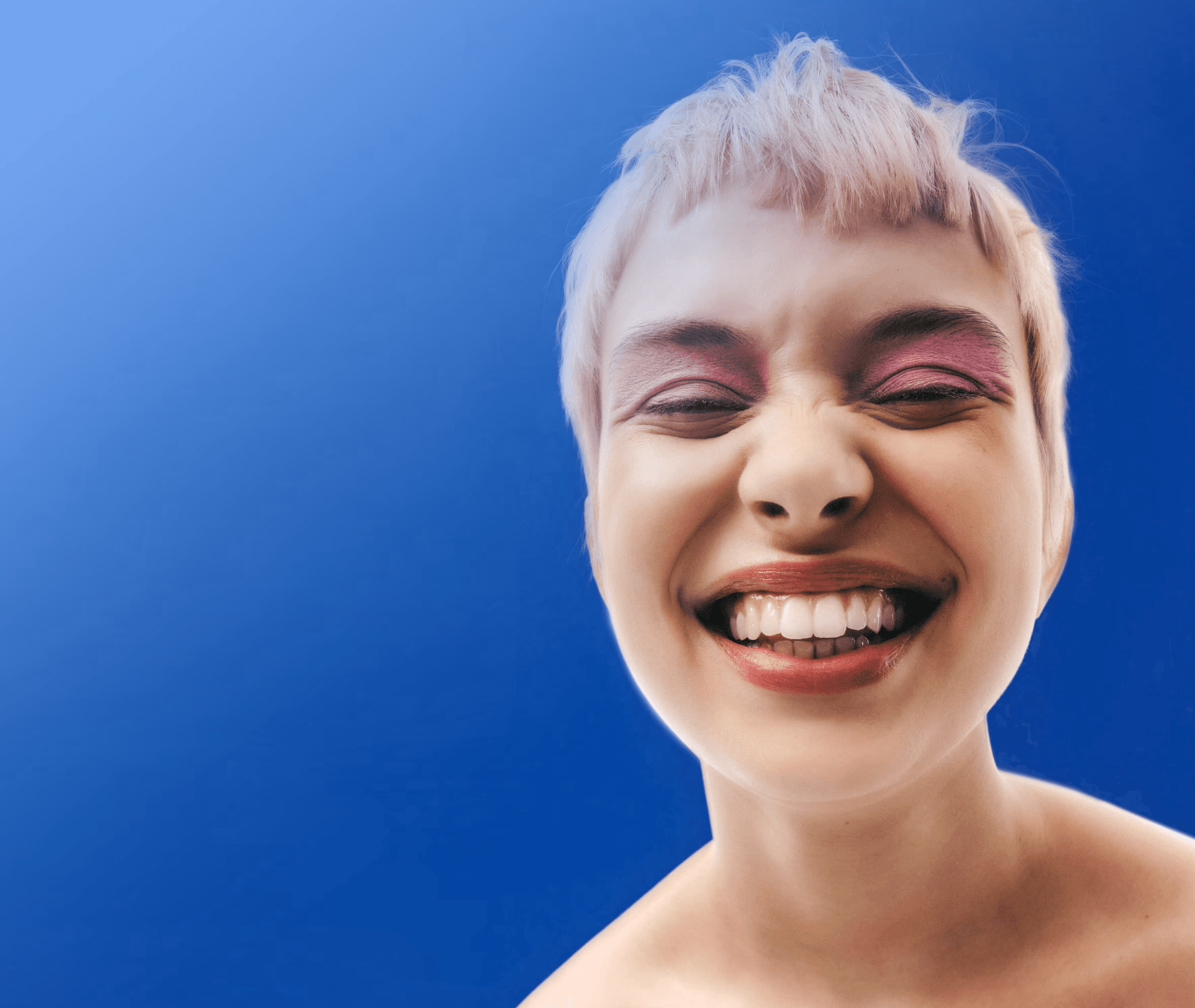 Expressive close-up portrait of a smiling person against a vivid blue background.