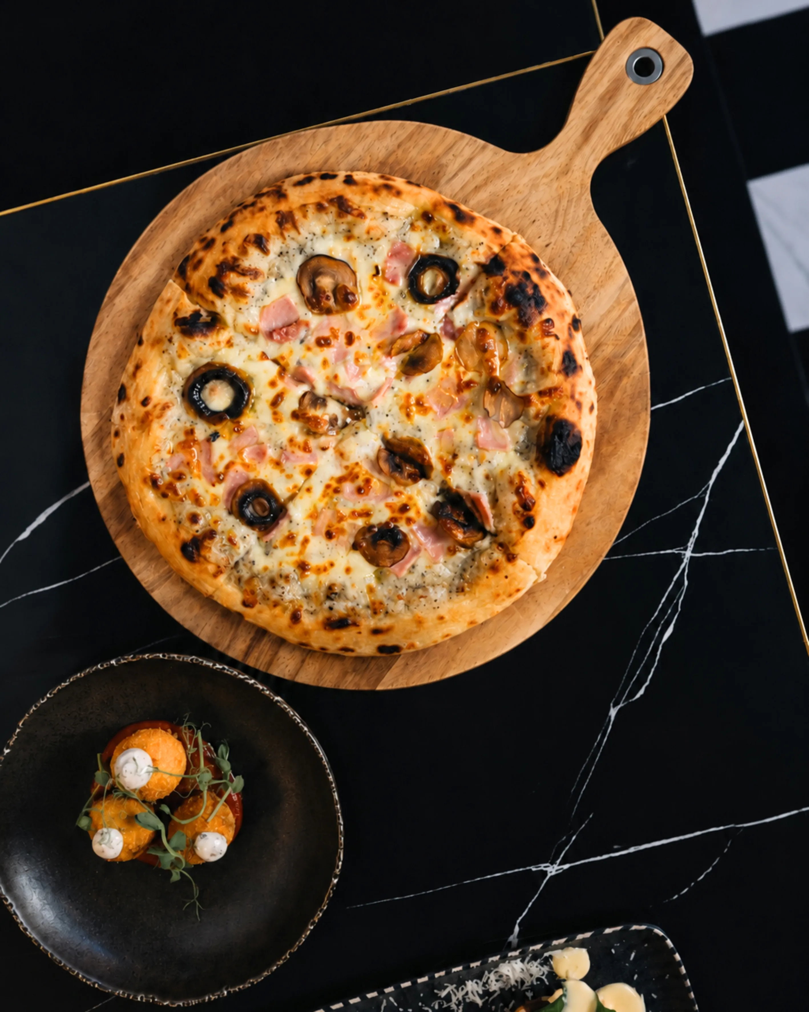 Pizza with mushrooms, olives, and ham on a wooden board