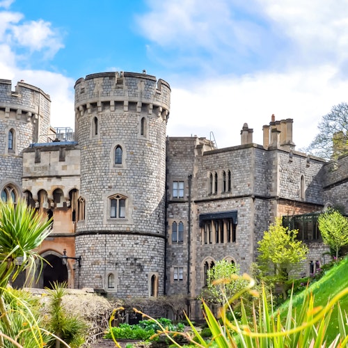 蓝天白云下，一座石砌城堡矗立其中，拥有圆形塔楼、拱形窗户，四周绿意盎然。