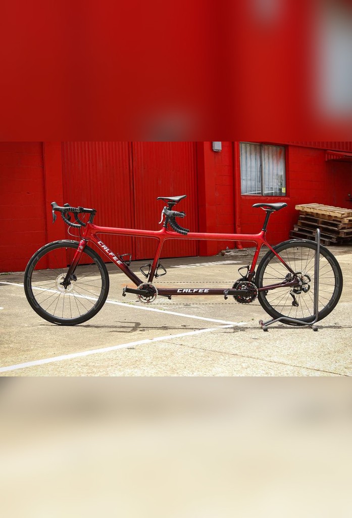 Photo of Lily's race tandem, Ruby Tuesday. The bike is red and black, with silver Calfee logos.