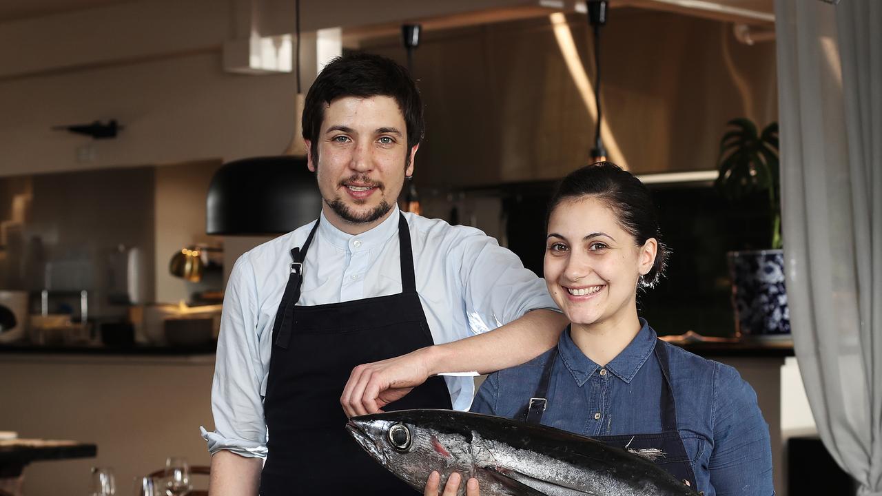 Two chefs pose with a large fish in a restaurant kitchen.