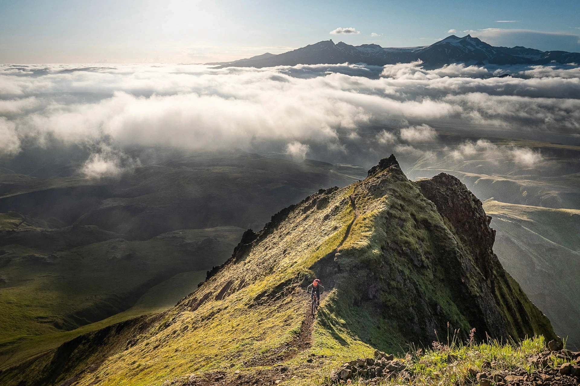 Cyclist riding along a narrow ridge above a blanket of clouds.