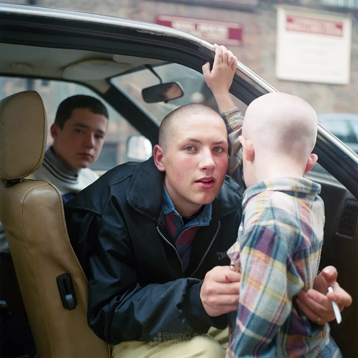 A young man seated in the front seat of a car, holding a child