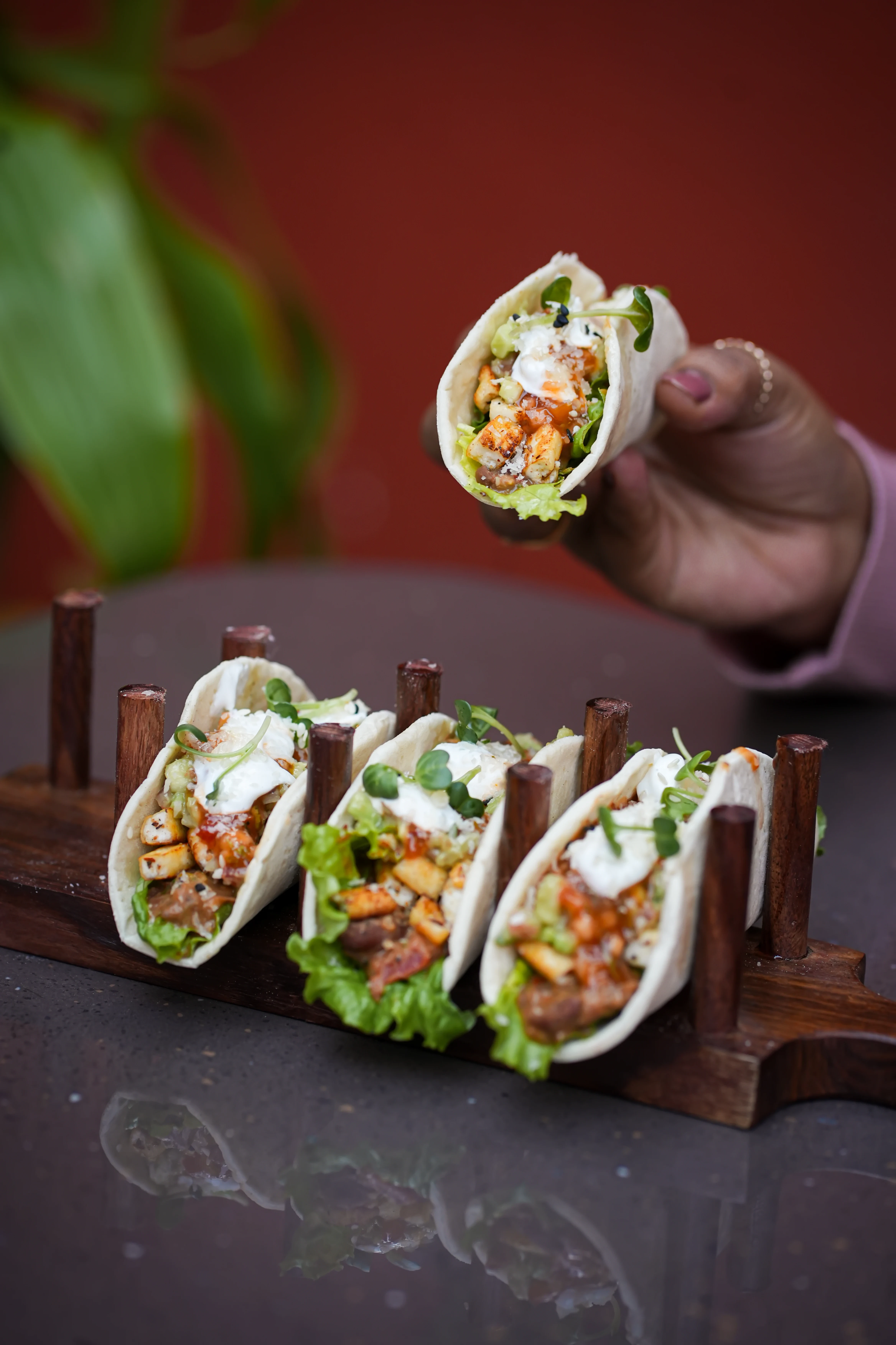 Tacos in a wooden holder and one being held