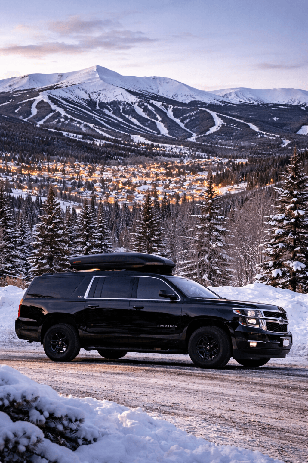 Black luxury SUV providing private car transportation in Breckenridge, Colorado with snowy mountain town and ski slopes in the background during winter.