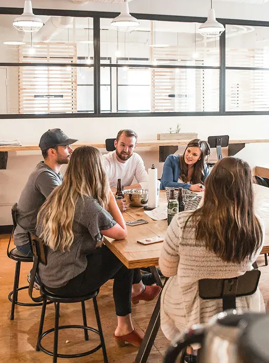 Team meeting in a modern open-plan office with people collaborating around a large wooden table.