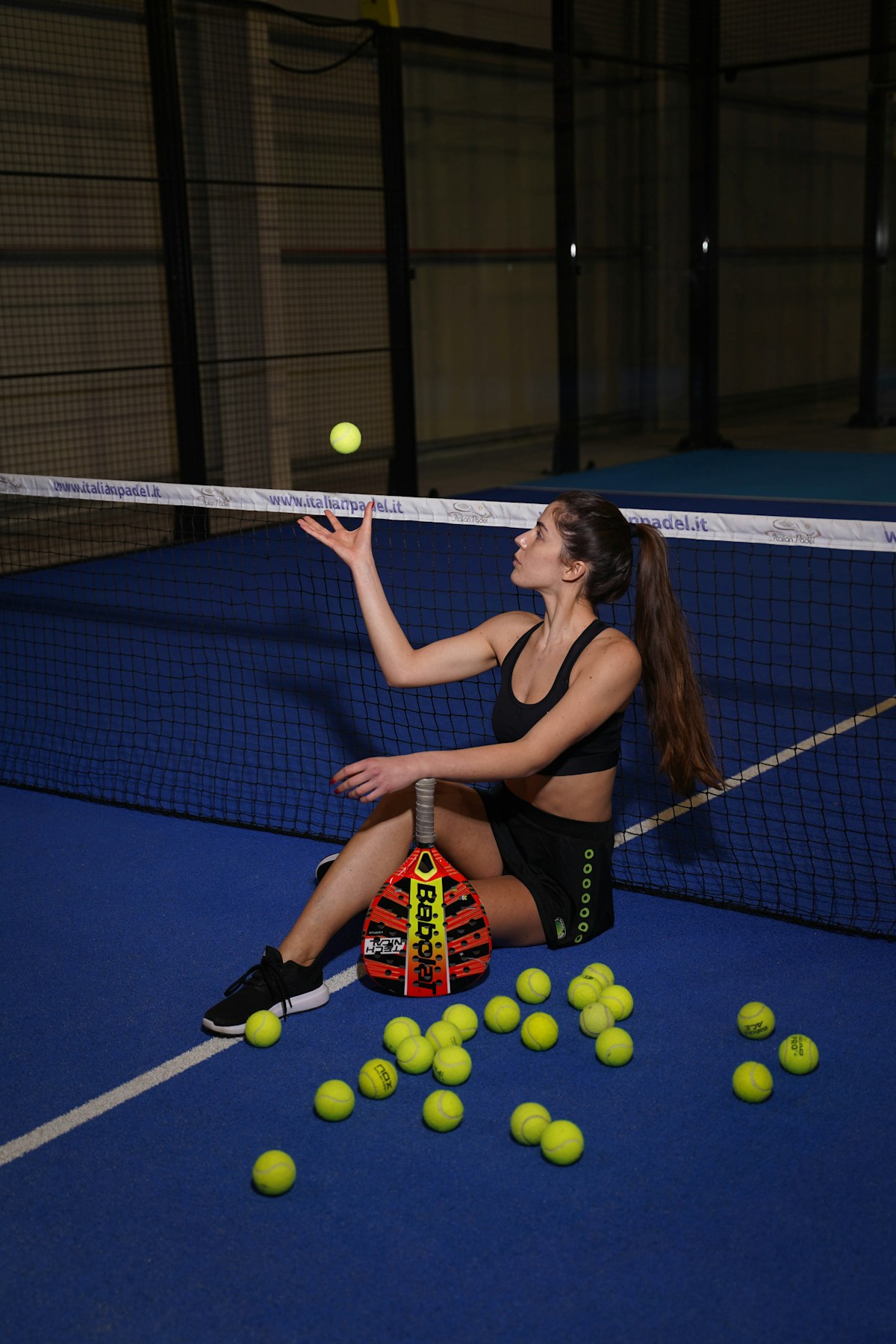 A player crouching on a blue padel court surrounded by balls