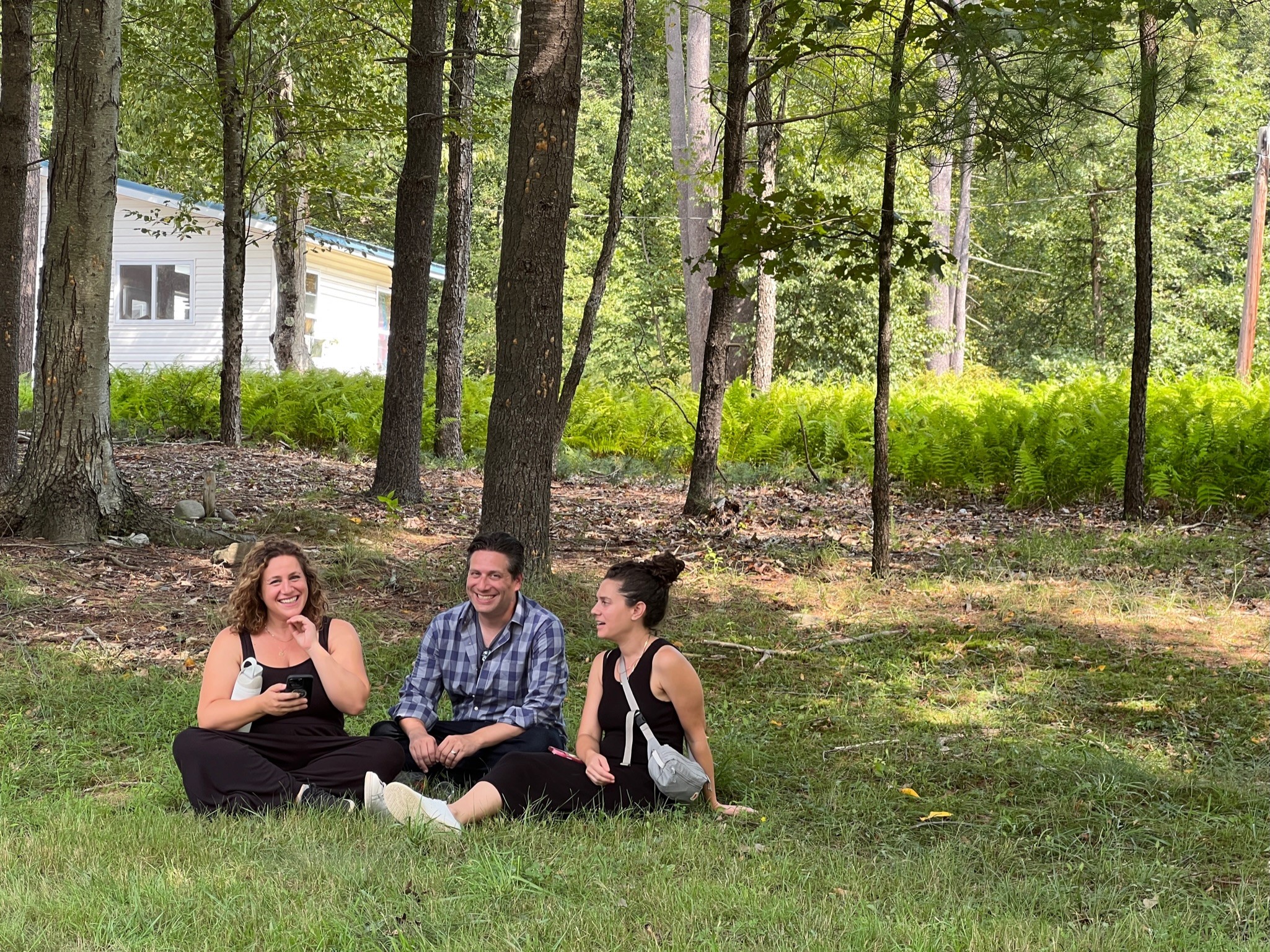 The Kormans sit on the grass in a peaceful, wooded area, laughing and talking together under tall trees.