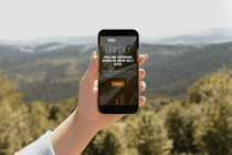 Mockup du site Léosky affiché sur un smartphone tenu en main, avec vue sur les montagnes et un chalet en arrière-plan.