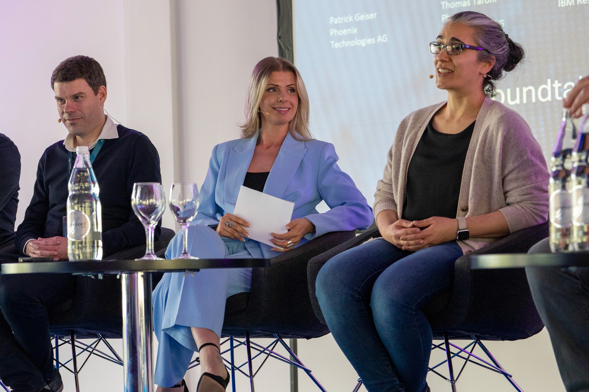 Moderatorin Désirée Lehmann hört aufmerksam einer Podiumsdiskussion zu, die sie führt und dabei einen hellblauen Anzug trägt.