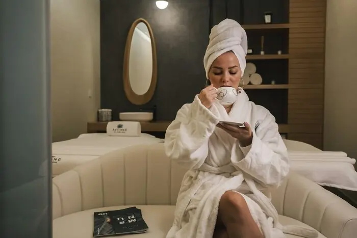 A woman in a white robe and hair towel sitting on a couch with a cup