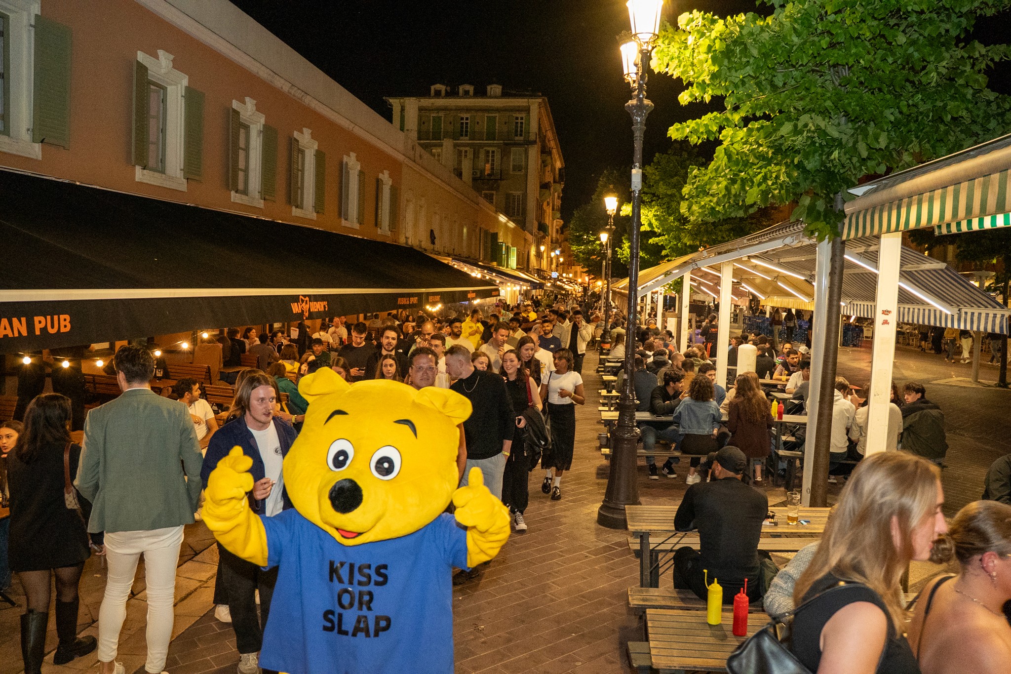 A pub crawl guide leading a group of travelers through the streets of Nice at night, smiling and talking as they move between bars.