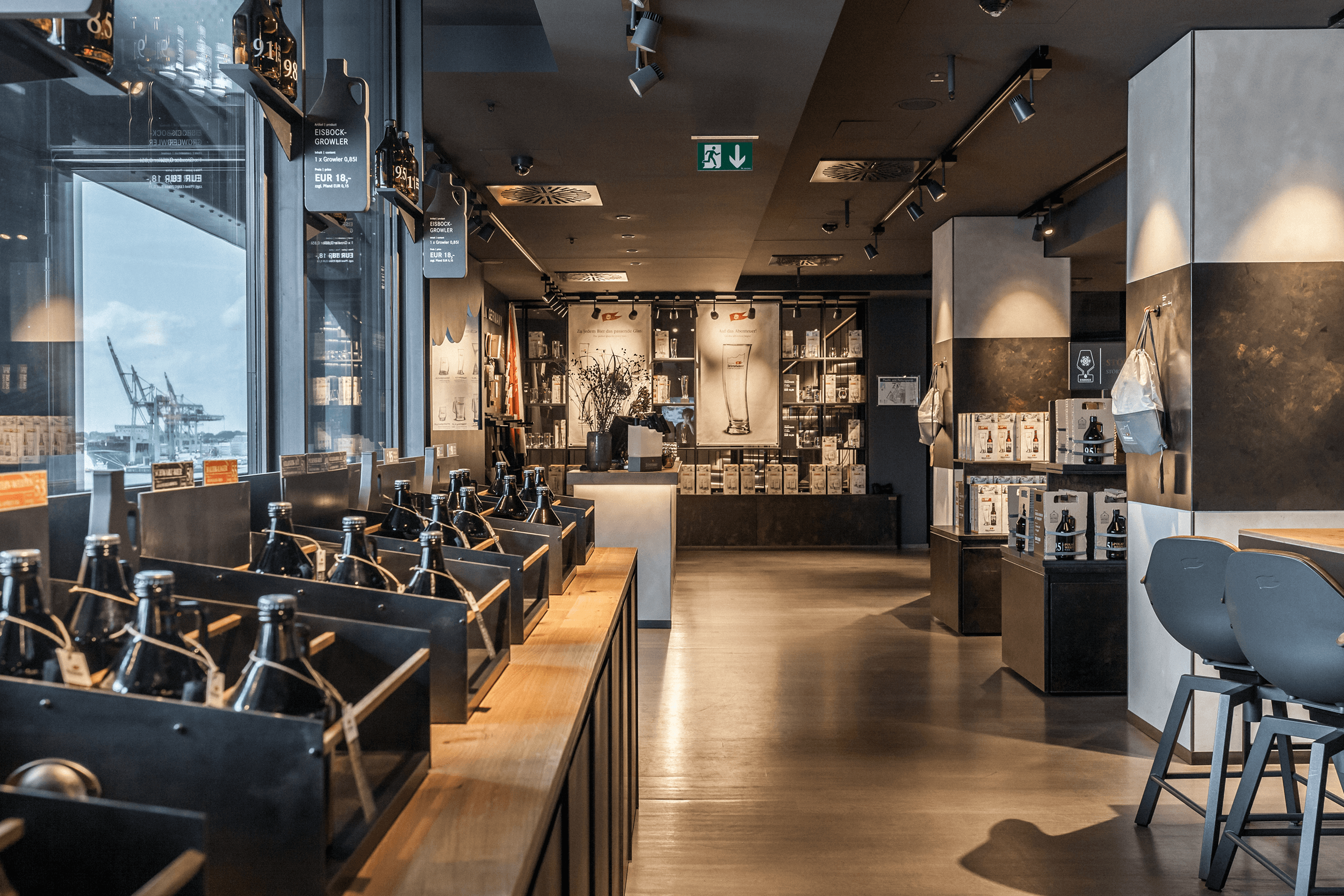 Bottles on a shelf in a store with industrial cranes outside.