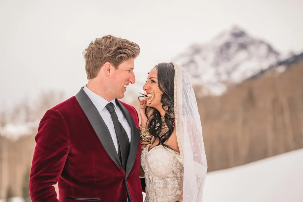Newlyweds smiling at each other with snowy mountains behind them