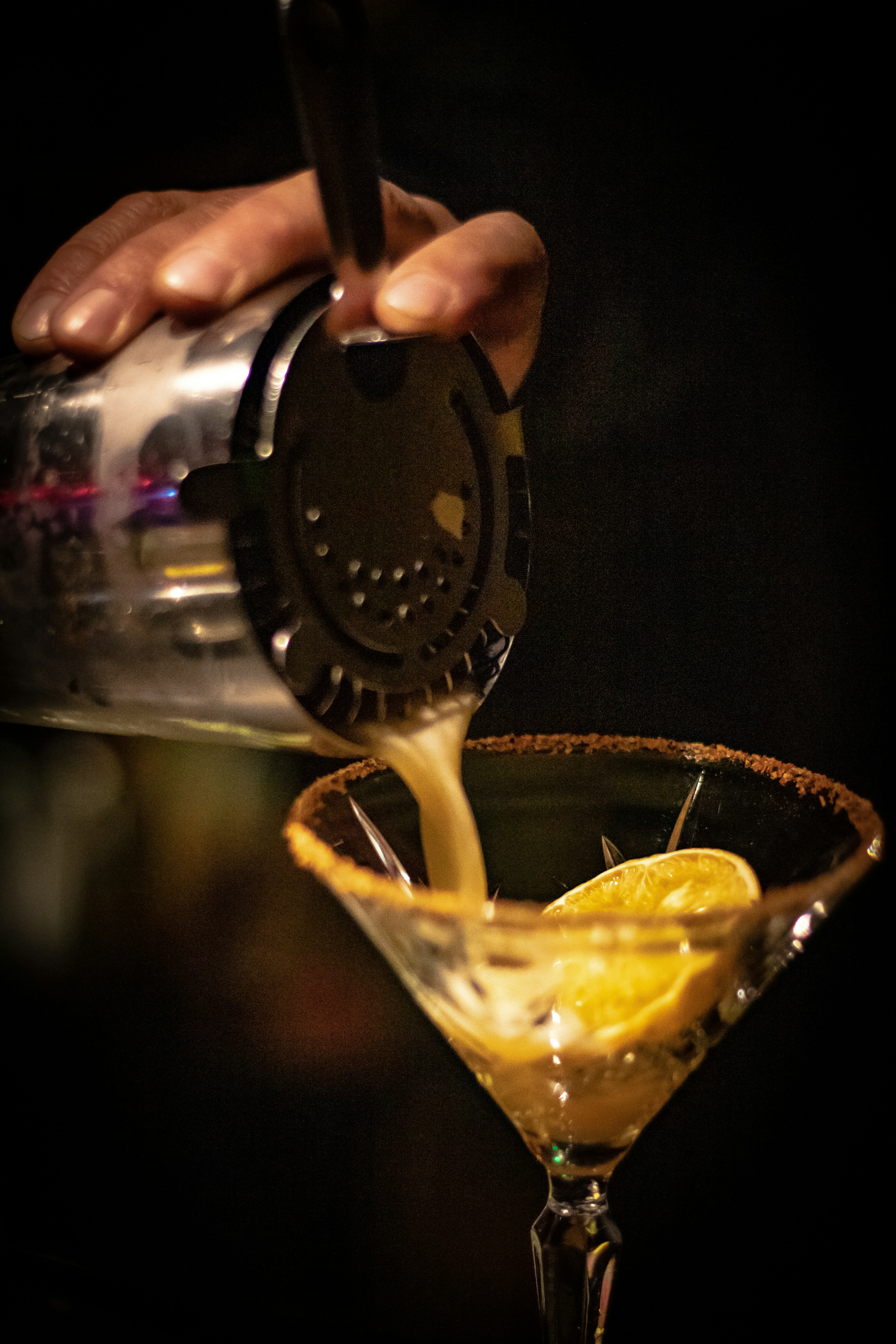 a person pouring a drink into a martini glass