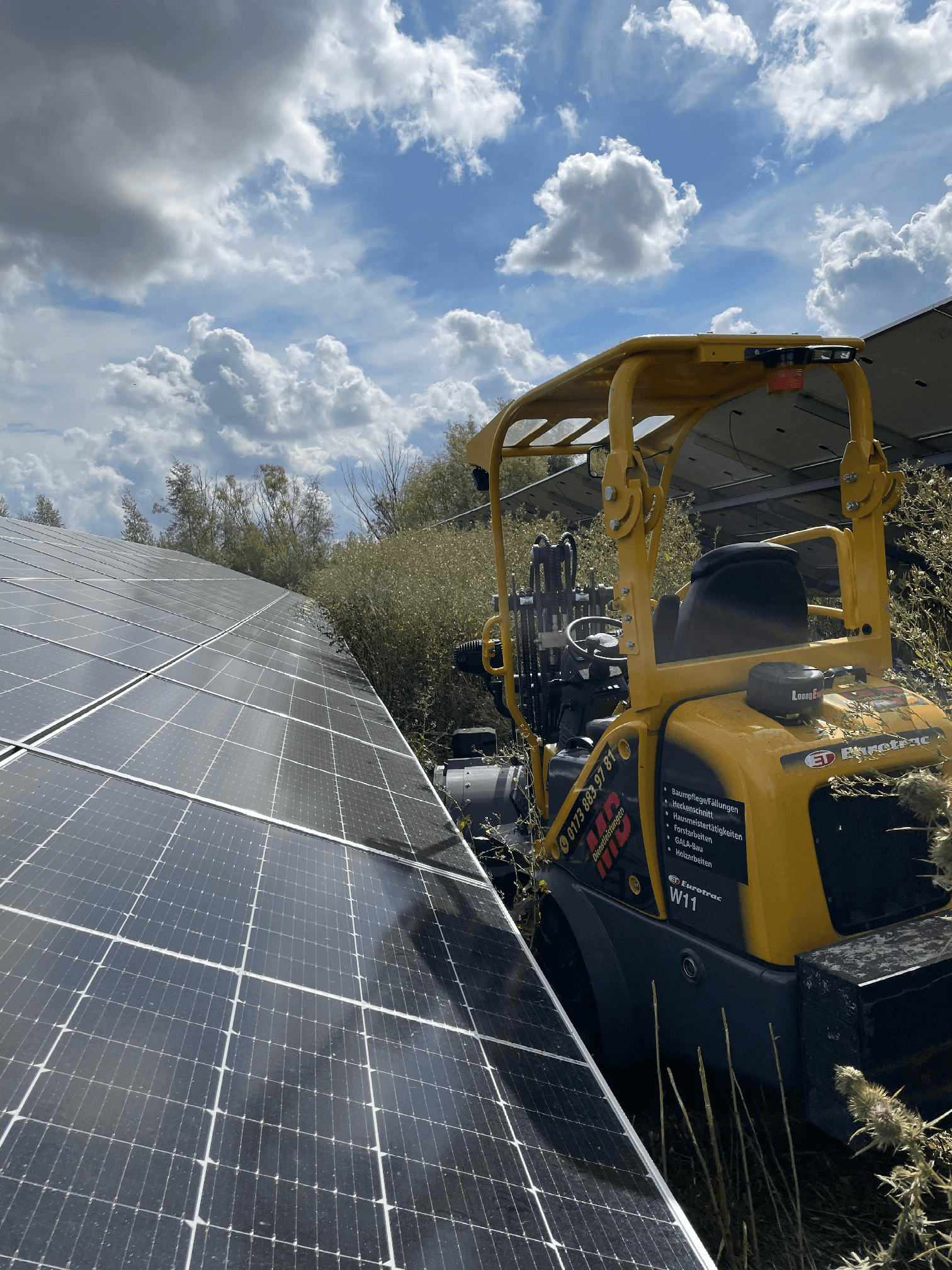 Mulcharbeiten mit Aufsitzmäher zwischen Solarpanel-Reihen bei sonnigem Wetter