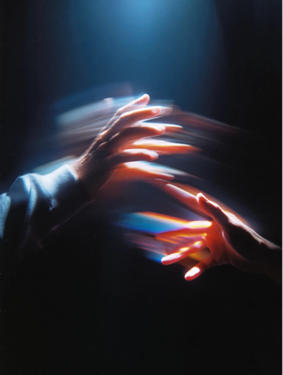 Blurry image of two hands reaching towards each other with streaks of light.