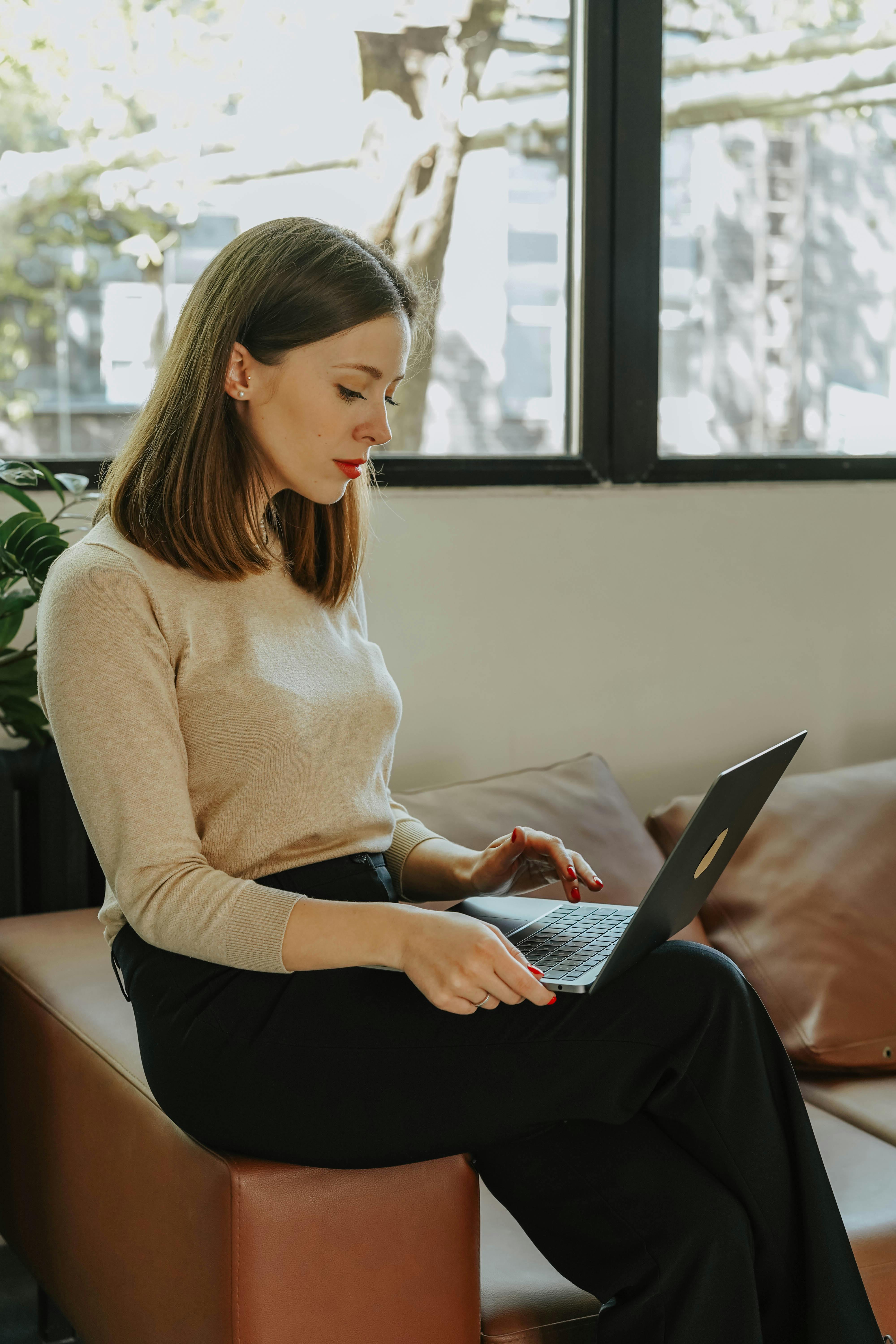  Woman Using a Laptop While Sitting on a Brown Sof