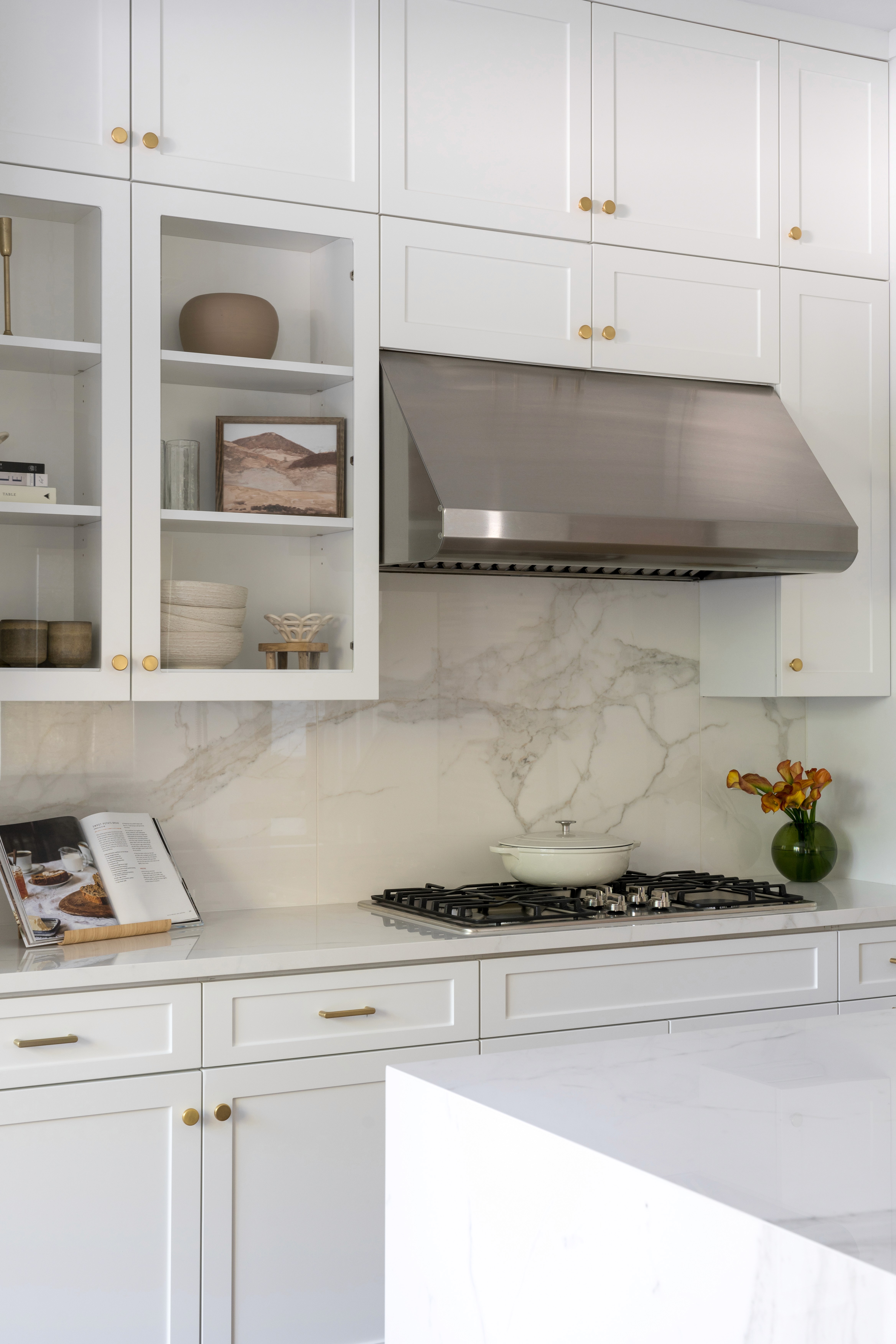 Neutral kitchen with white cabinets, brass finishes, and stainless steel range hood by Jubilee Interiors in Arcadia, California