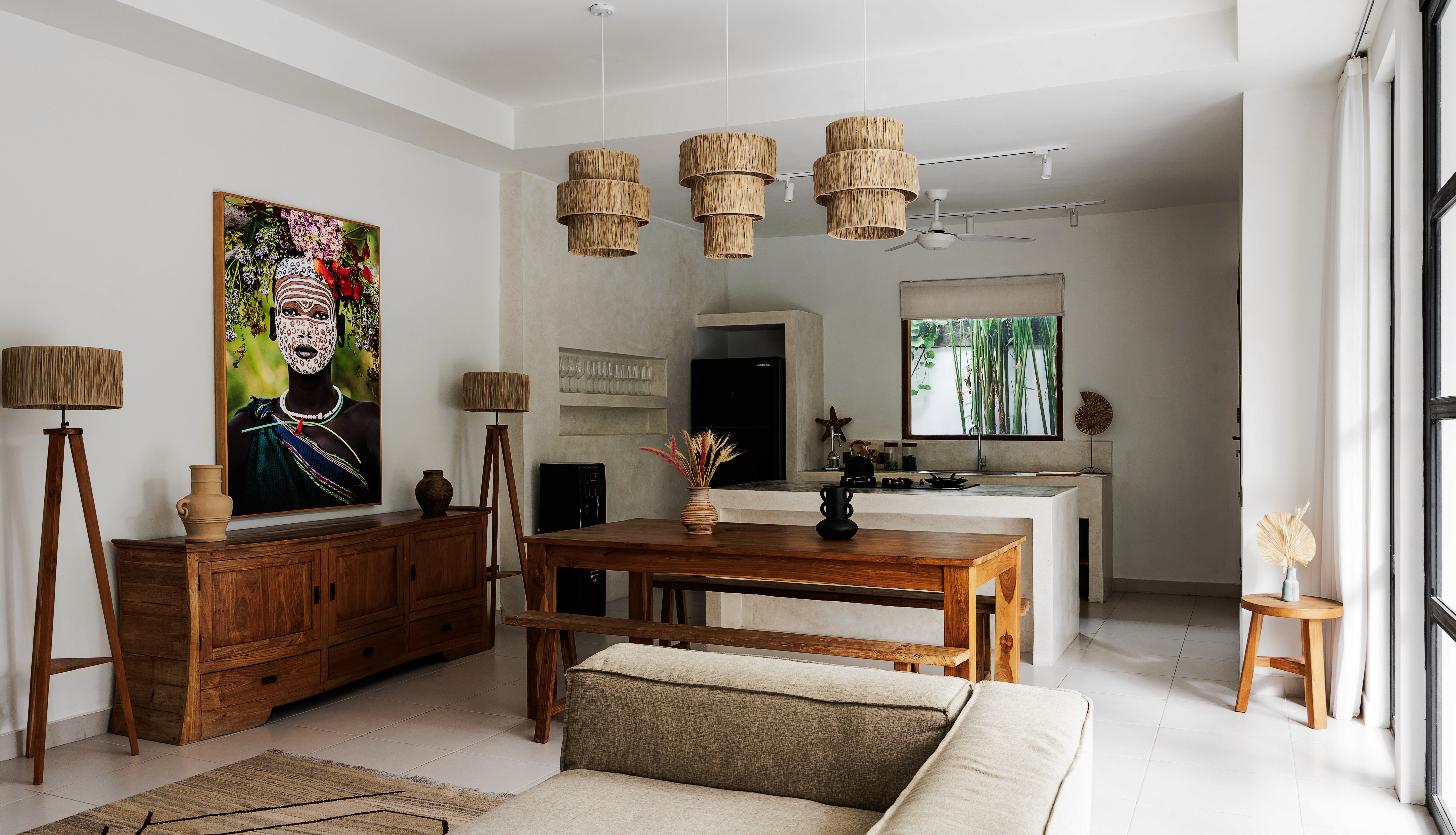 Modern tropical kitchen and dining area with natural wood furniture, woven lighting, and vibrant wall art.