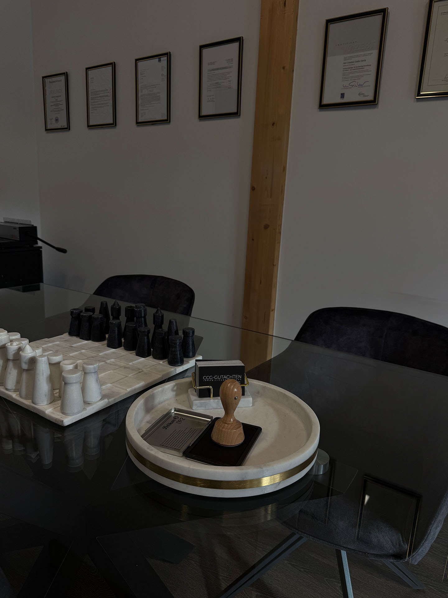 Büro von CCG-Gutachten mit gerahmten Sachverständigen-Zertifikaten, Schachspiel und Stempel