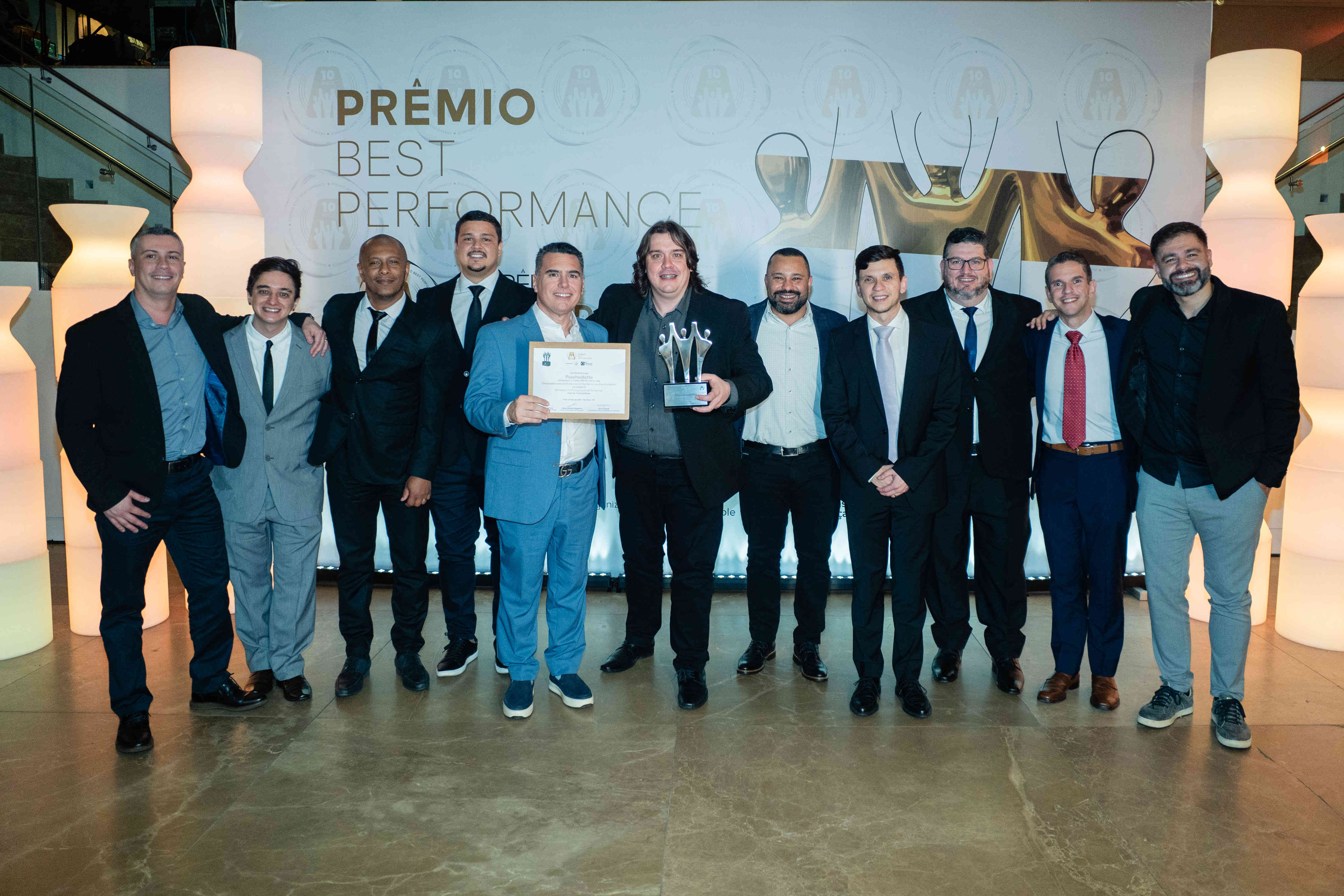 Executivos da Paschoalotto posando com troféu prata e certificado no palco do Prêmio Best Performance 2025
