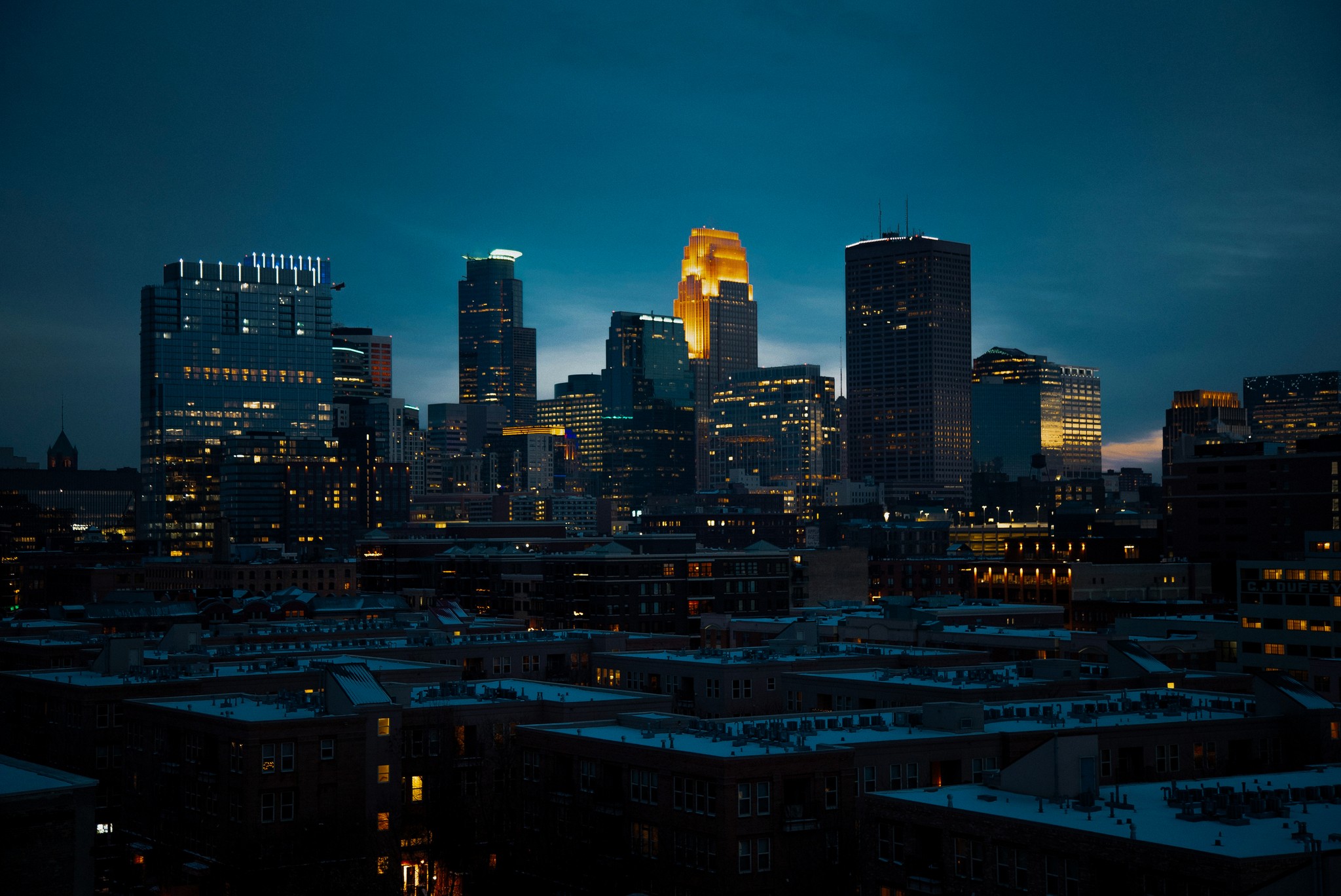 a twilight Minneapolis cityscape with illuminated skyscrapers and a darkening sky.
