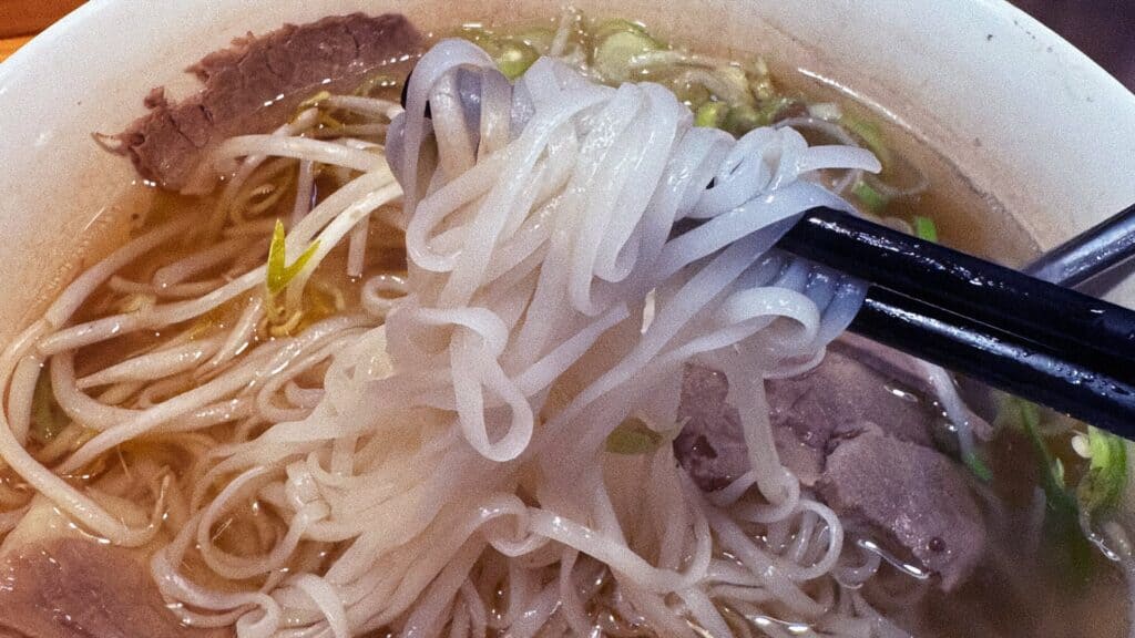 Cận cảnh sợi phở tươi trắng mềm được gắp lên bằng đũa từ tô phở bò tại quán Việt ở Hàn Quốc