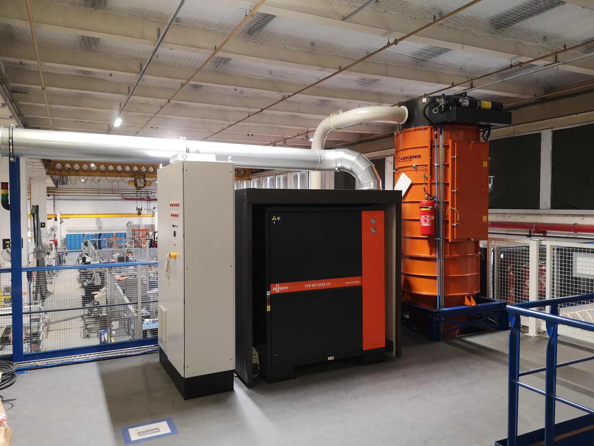 Centrale d’aspiration dans un atelier : cyclone orange, pompes, réseau de tuyauterie et armoire électrique de commande.