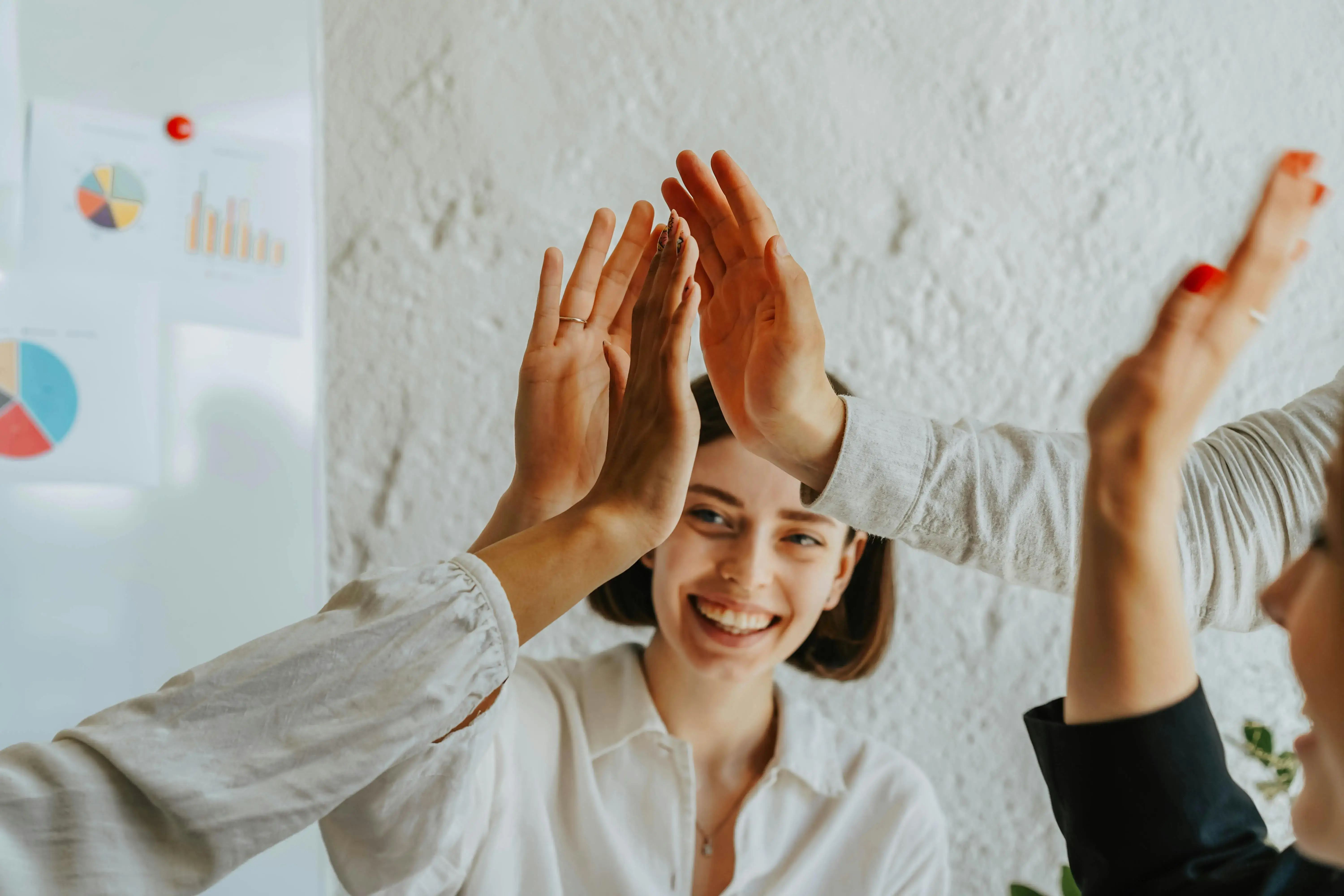 Two professional women smiling and giving each other a high-five in an office