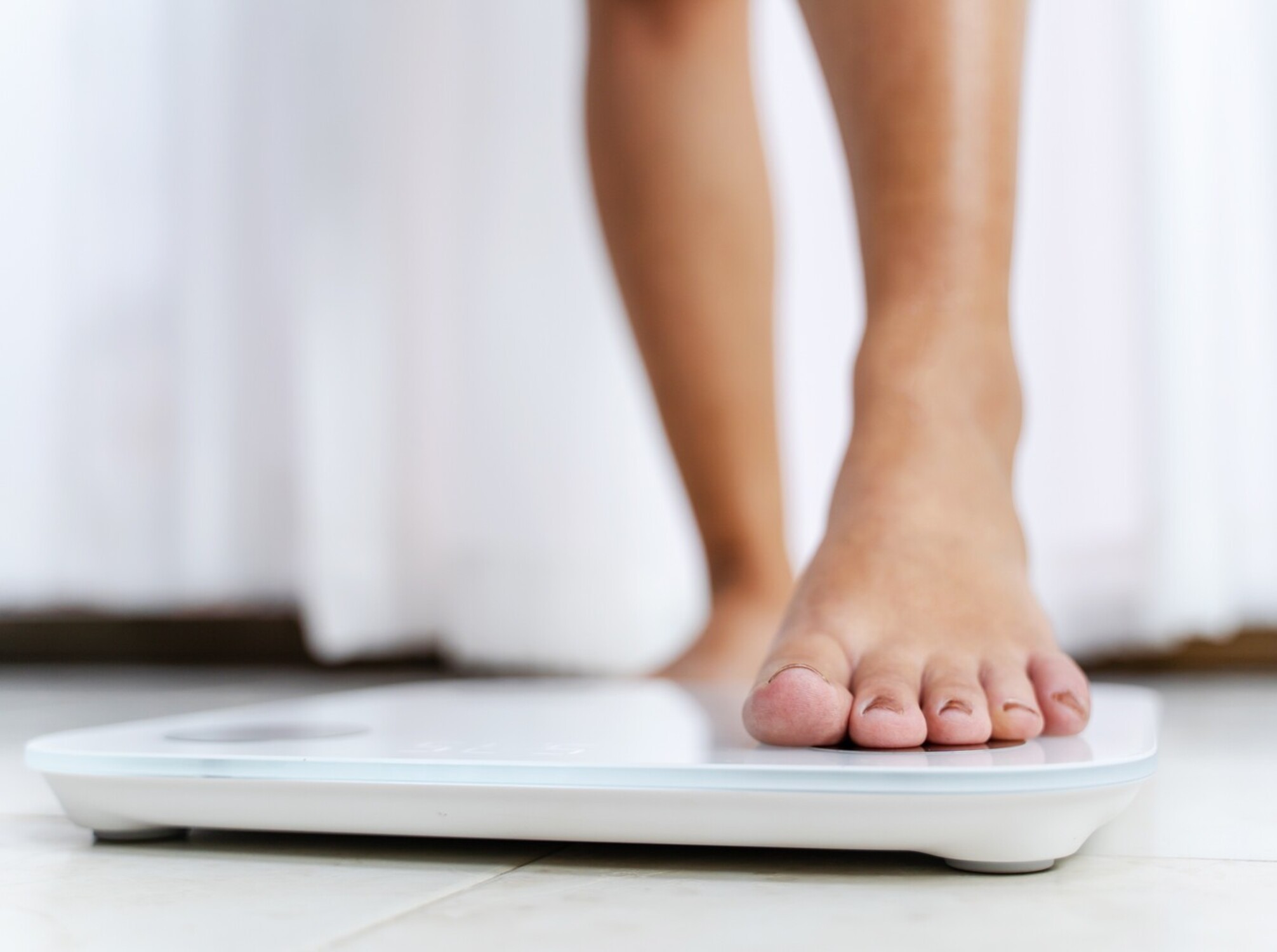 woman stepping onto a scale in her bathroom to check her results from her yoga routine for weight loss