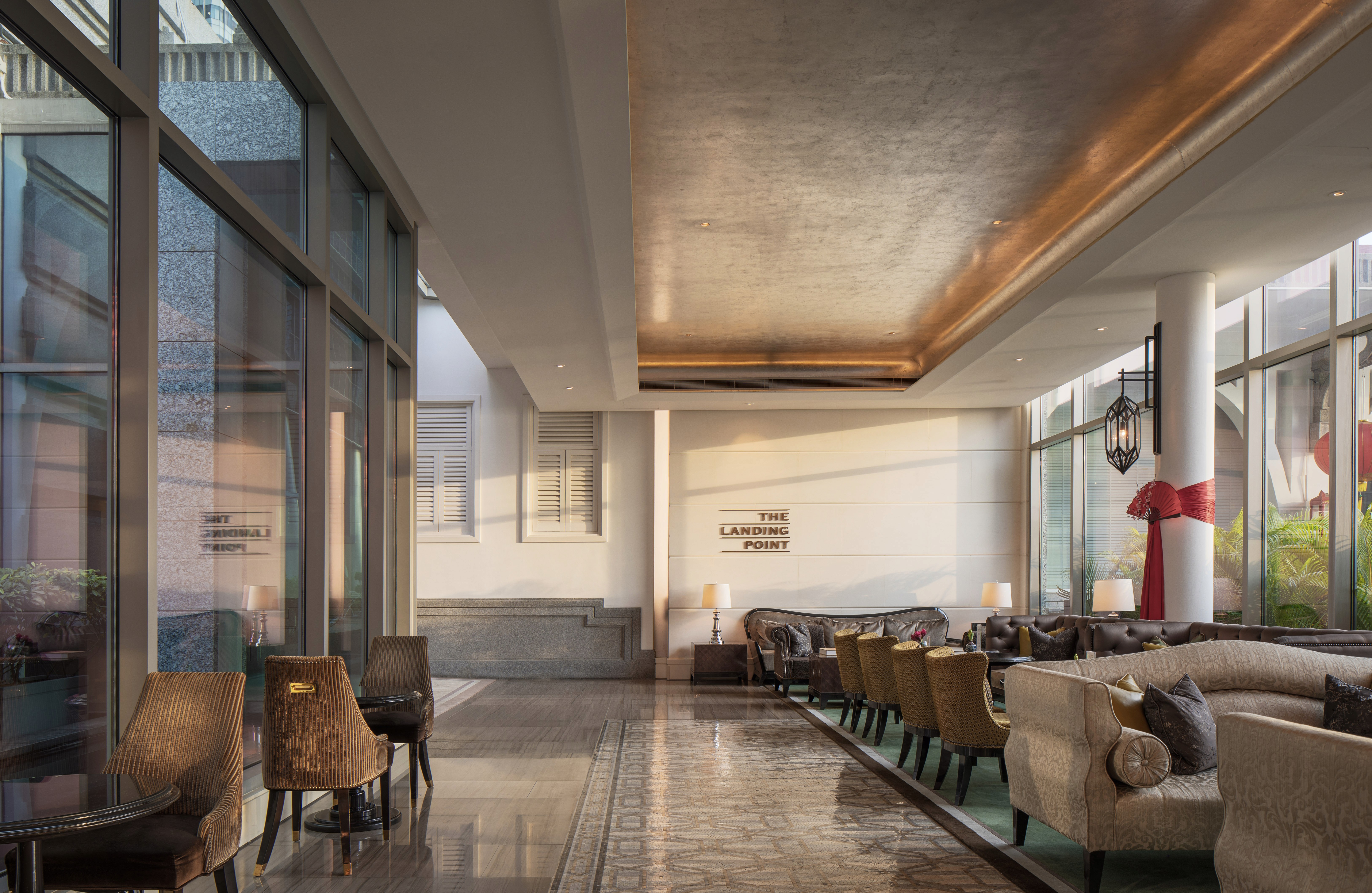 A high-end hotel lobby featuring a sophisticated mix of plush seating, warm lighting, and large glass windows opening to an exterior view, creating a welcoming and refined atmosphere.