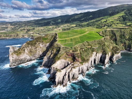 green grass field on rocky mountain beside sea under white clouds and blue sky during daytime