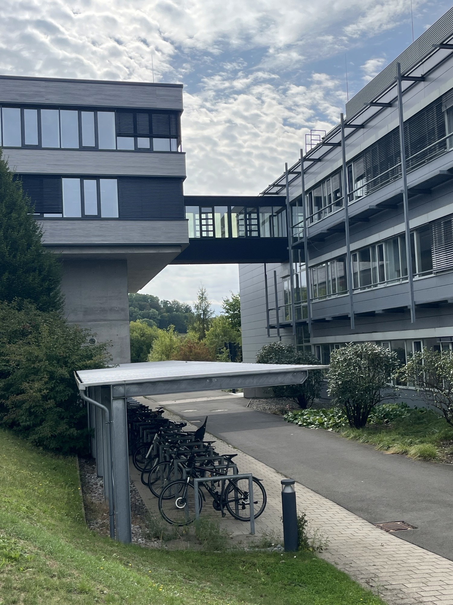 Glasgangverbindung zwischen zwei Gebäuden und Fahradabsteller vor den Gebäuden