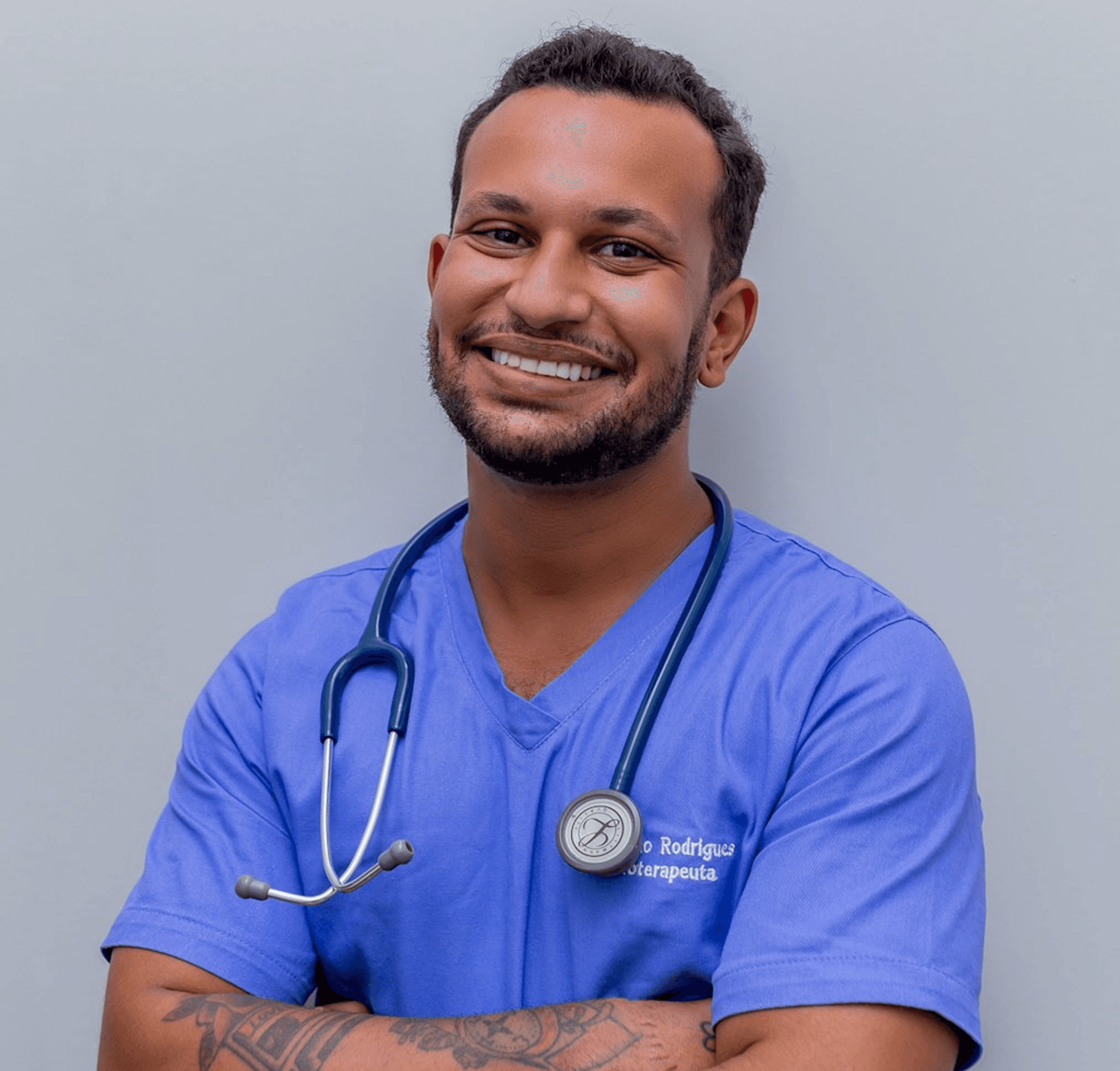 Healthcare professional in blue scrubs with stethoscope, standing against light gray background