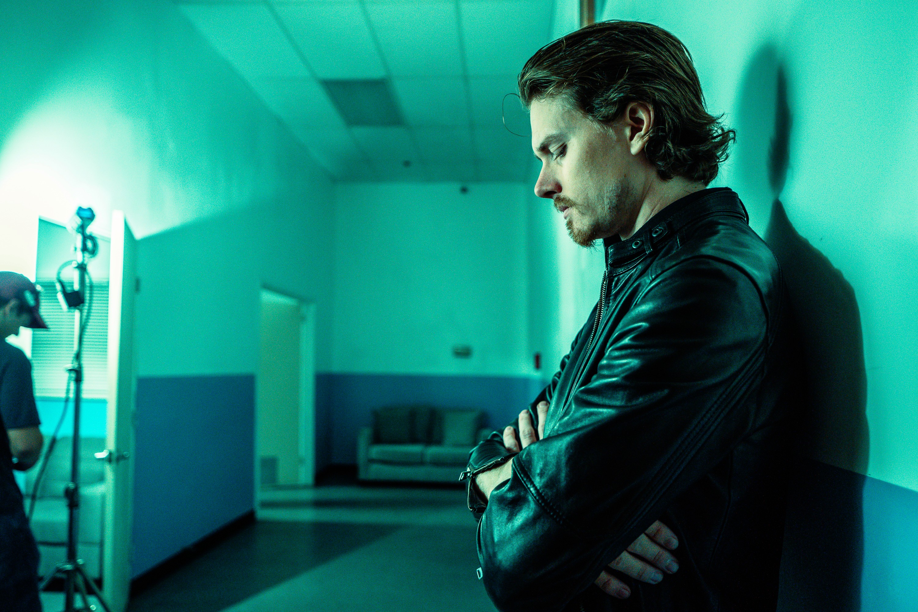 Ryan Joseph leaning against a wall in teal light, behind the scenes of Pathogen.